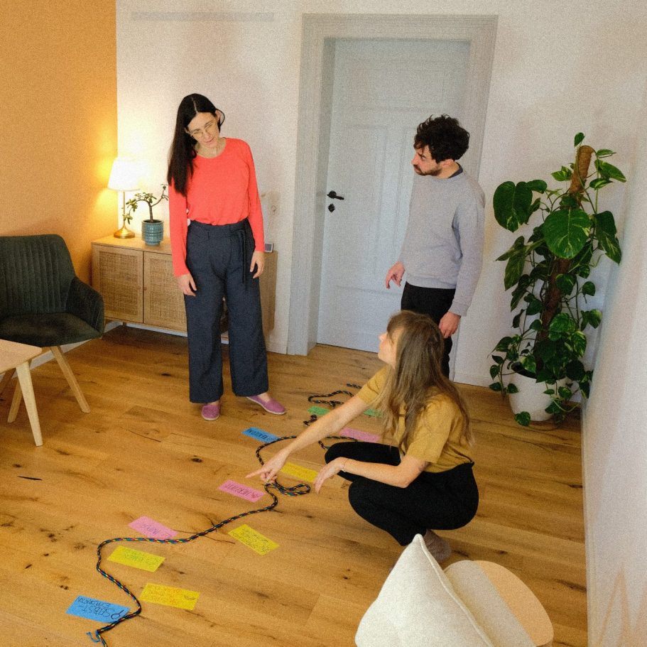Paarberatung Drei Personen - die Beraterin und ein Paar - arbeiten in einem Raum. Auf dem Boden liegt ein Seil mit Moderationskarten.